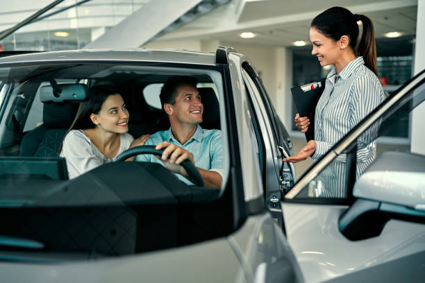 Sales advisor speaking with a couple seated in a car at a dealership